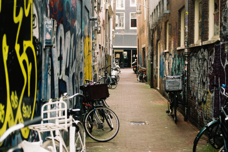 Steeg in Amsterdam met fietsen tegen muren vol met graffiti en stickers